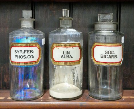 Three large early 20th century 'label under glass' apothecary bottles and stoppers, each of cylindrical form with faceted rec