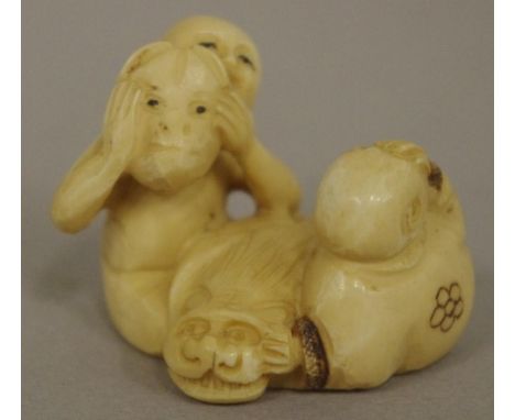 Antique Japanese ivory figural group netsuke depicting a masked man and lying laughing man with a cat in between, red sealed 