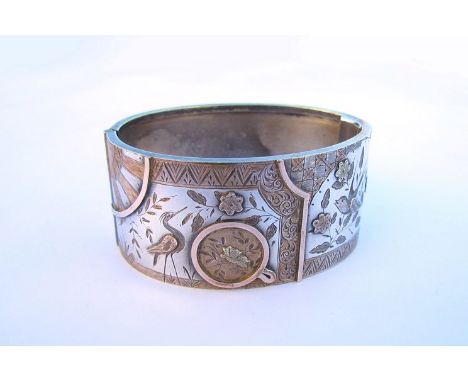 A silver gold stiff hinge bangle with panels depicting sunburst and crane and bird in flowers, unmarked