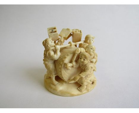 A 19th Century carved ivory netsuke of figures around a drum, red insert signed panel to base. 6cm tall 