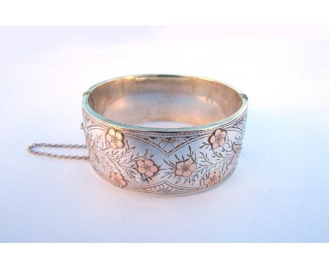 A silver gold stiff hinge bangle with engraved foliage and gold flowers and leaves with safety chain, Birmingham