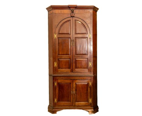 A fine George III period mahogany Corner Cupboard, the breakfront moulded cornice with a female mask in relief to the frieze,