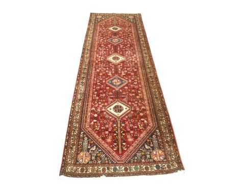 A hand knotted woolen Abadeh runner rug, with a red field and stylised border, 85 by 292cm.