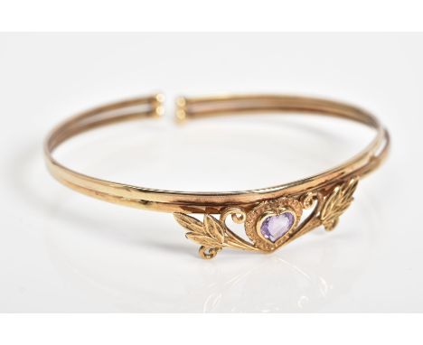 AN AMETHYST SET BANGLE, set with a central heart shaped amethyst within a floral detail panel, to the double banded open bang