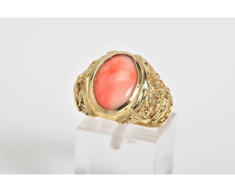 A CORAL SET RING, the yellow metal ring designed with a central oval coral panel within a collet mount and embossed detail sh
