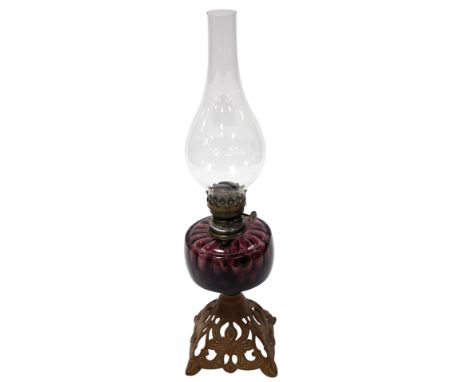 An early 20thC cast iron and brass oil lamp, with an amethyst glass reservoir, glass chimney, raised on a foliate scroll base