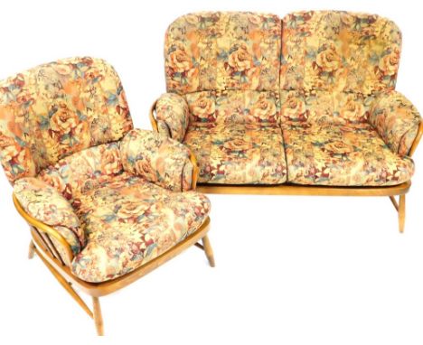 An Ercol Jubilee dark elm and beech cottage two seater sofa and matching armchair, each with a stick back and floral upholste