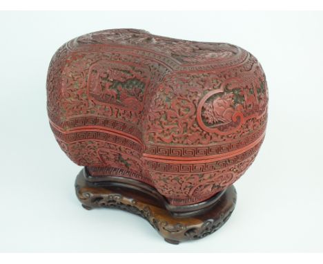 A Chinese cinnabar lacquer ingot form box and cover on a carved hardwood stand, early Qing Dynasty, the cover with a central 