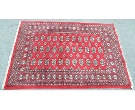 A mid 20th century Persian Bokhara carpet floor rug. The rug having red ground, with a series of repeated gul style medallion