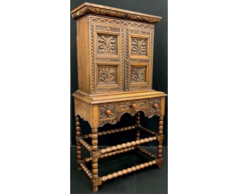 A Jacobean Revival oak hall cupboard, the cornice, doors, and drawer fronts carved in deep relief with scrolling leaves, bobb