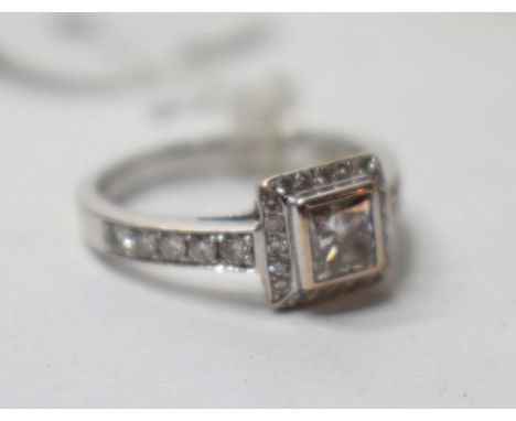 An 18ct white gold and diamond ring, the central princess cut stone within a brilliant cut diamond halo, and flanked by diamo