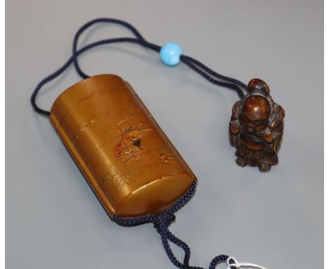 A Japanese gold lacquer four case inro with relief tiger and a hotei carved wood netsuke and blue glass ojime