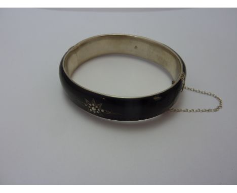 AN EARLY 20TH CENTURY BANGLE, with black enamel and seed pearl detail to the decorative clasped safety chain