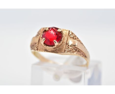 A RING, set with a circular cut red paste within a four claw setting to the textured surround and shoulders, ring size M1/2, 