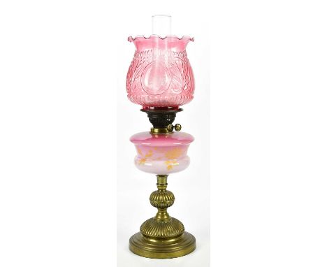 An early 20th century oil lamp with cranberry glass shade above cranberry and milk glass resevoir with gilt bamboo effect dec