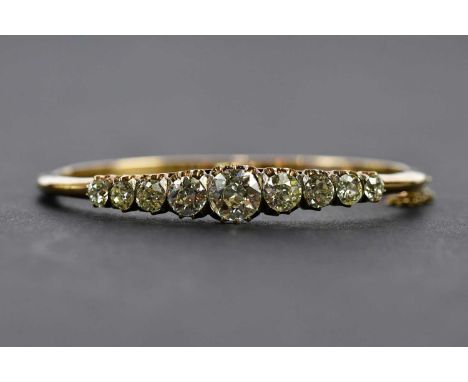 A stunning yellow metal and diamond set hinged bangle with nine graduated old cut diamonds centred with a stone weighing appr
