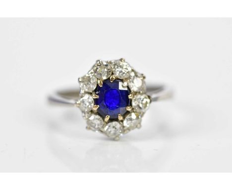 An 18ct white gold sapphire and diamond oval flower head ring centred with a claw set oval sapphire within a border of nine d