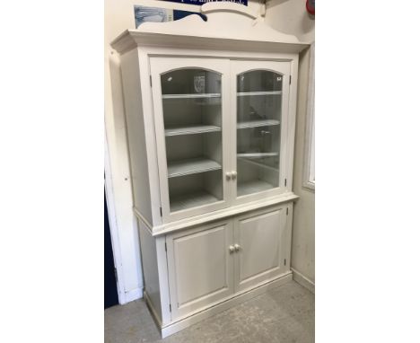 A pair of modern white painted bookcase cabinets with fretwork pediments over two arched panelled glazed doors enclosing shel