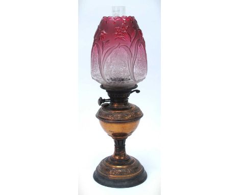 Oxidised copper oil lamp circa 1900 of circular form with iron base, cranberry embossed and etched ovoid glass shade funnel, 