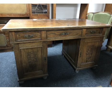 An early 20th century oak pedestal desk with carved panel doors 