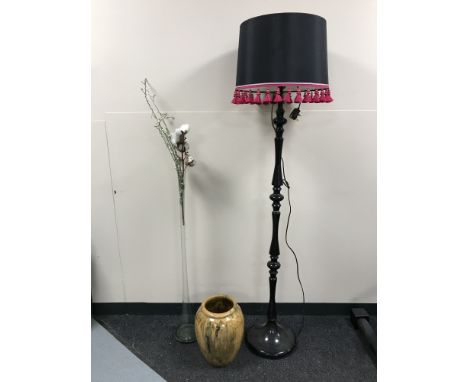 A black standard lamp with shade together with a tall glass vase containing dried flowers and a bamboo vase