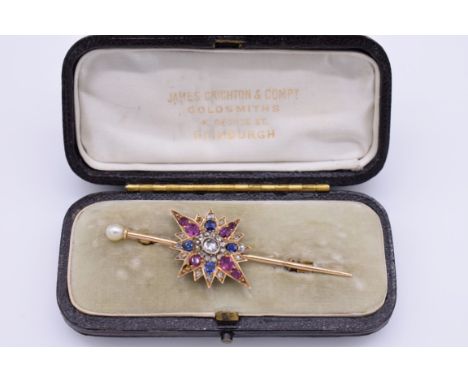 A sapphire, ruby and diamond yellow metal starburst cravat pin, having pearl finial, in fitted case, 6.5cm long, 6.4g total w