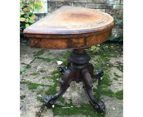 A Victorian walnut demilune card table, hinged top enclosing a baize lined playing surface, turned column carved with leaves,