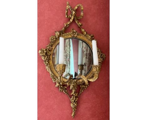 An ornate gilt plaster wall mirror with bows and floral garlands, 2 candle sconces. 58cm h x 34cm w. 