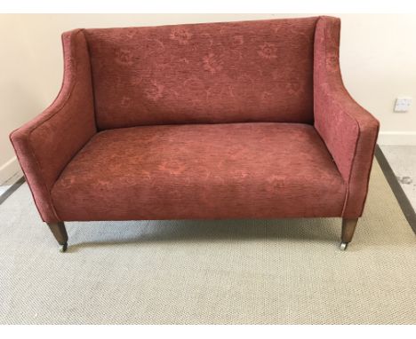 An Edwardian upholstered swept arm two seat sofa on square tapered front legs to castors, 140 cm wide x 74 cm deep x 87 cm hi