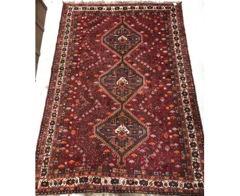 A Persian carpet, the central panel set with three repeating medallions on a red ground, within a stepped red, brown and crea