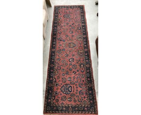 A Persian runner, the central panel set with all-over scrolling foliate decoration on a pink ground, within a stepped pink an