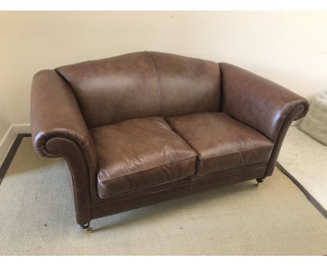 A Laura Ashley "Gloucester" brown leather upholstered scroll arm two seat sofa on turned front legs to castors,170 cm wide x 