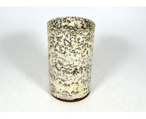 † A Lucie Rie cylindrical stoneware vase, white pitted with flowing glaze. Manganese elements in the body creating a brown sp