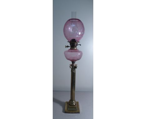 A late 19th/early 20th Century cranberry glass oil lamp with globular floral etched shade and reservoir over a brass Corinthi