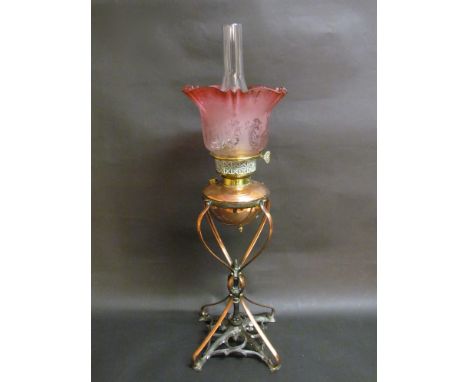 An Art Nouveau oil lamp with copper stylistic base and reservoir with an etched cranberry shade 