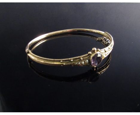 A 9ct gold Edwardian bangle with round cut amethyst flanked by graduating seed pearls with ball finials, and safety chain 