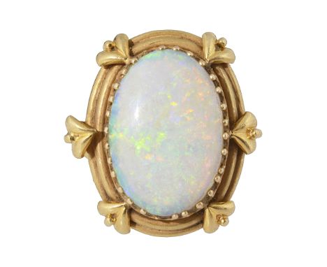 An oval opal ringoval cabochon opal, claw-set within a yellow metal foliate border, with trifurcated shoulders and a reeded s