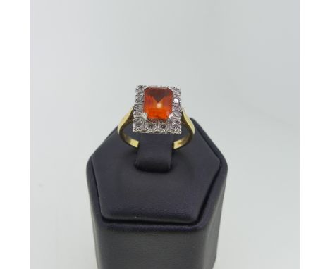 A fire opal and diamond cluster Ring, the central emerald cut opal 8mm x 6mm surrounded by twelve diamond points, all mounted