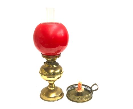 A brass oil lamp with glass chimney and red glass shade, 49cm high overall; together with a brass candle holder with pierced 