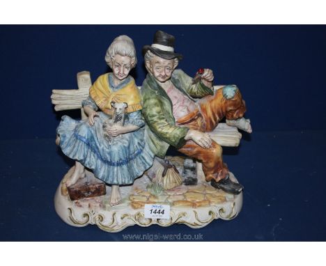 A large Capo di Monte style ornament of a tramp and an elderly lady sitting on a bench.