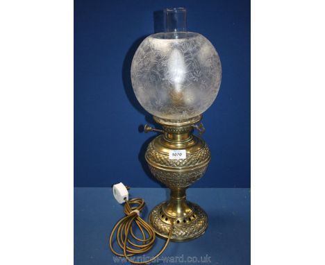 A brass oil Lamp converted to electric with decorated panels around the base and lamp, having a globular glass shade etched i