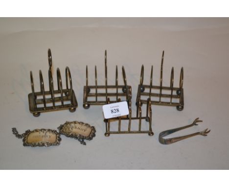 Pair of silver decanter labels, four plated toast racks and a pair of sugar tongs