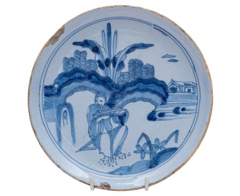 A late 17th century English blue and white delftware saucer dish painted and trecked with a chinaman seated beneath rocks and