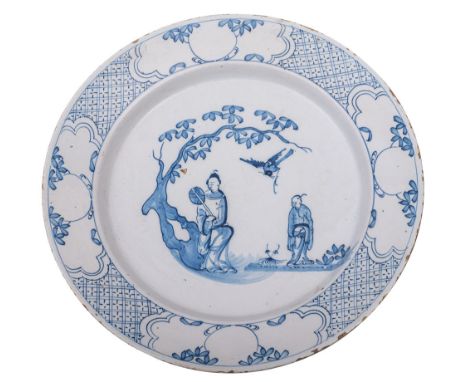A Bristol blue and white delftware charger painted with oriental figures in a garden, a large bird flying above, the rim with