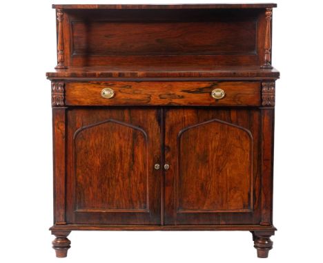 A George IV rosewood side cabinet or chiffonier, circa 1825; with raised shelf above twin turned supports and a panel back to