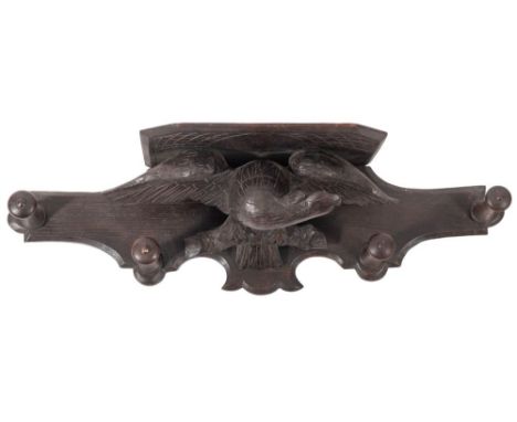 A carved and stained oak bracket and peg rail, early 20th century; the shelf with canted front corners, above a stylised spre