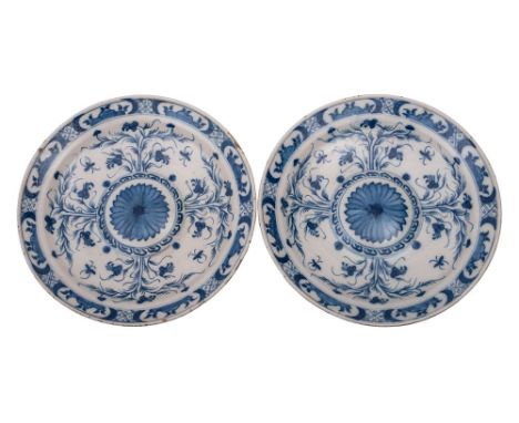 A pair of Dutch blue and white delftware chargers with central bosses each painted with a flowerhead surrounded with stems of