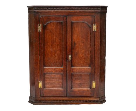 A George III oak hanging corner cabinet, last quarter 18th century; the cornice and blind fretworked frieze above two panel d