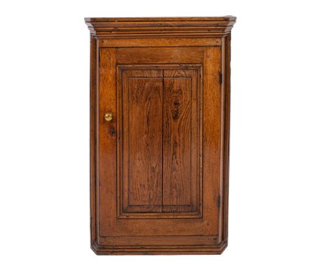 A George III oak hanging corner cupboard, circa 1800; with moulded cornice above a panel door, canted side angles and a mould