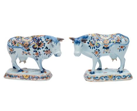 A pair of Dutch delftware cows modelled standing four square, head tilted to one side, on a rectangular base and decorated wi
